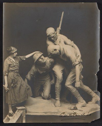 Woman in early 20th-century attire interacting with war sculpture of two soldiers.