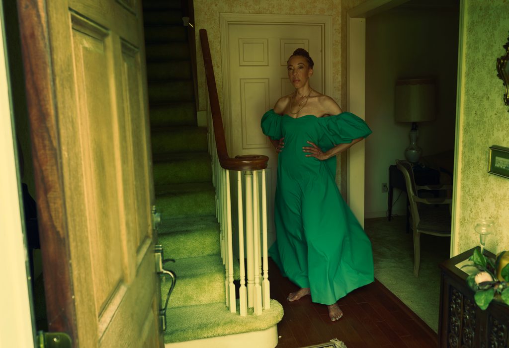 Photo of woman in a green off shoulder dress next to a stairwell shot through a doorway