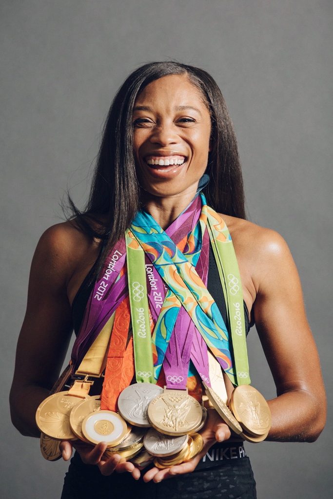 Smiling person with long hair holding London 2012 and Rio 2016 Olympic medals.