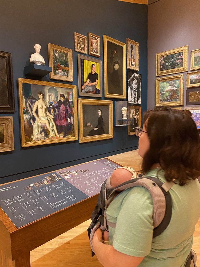 a visitor carries a baby while looking at art on the salon hang wall