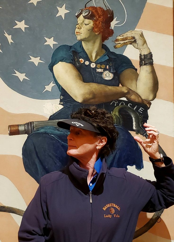 a woman visitor poses in front of rosie the riveter in the same pose the subject is in