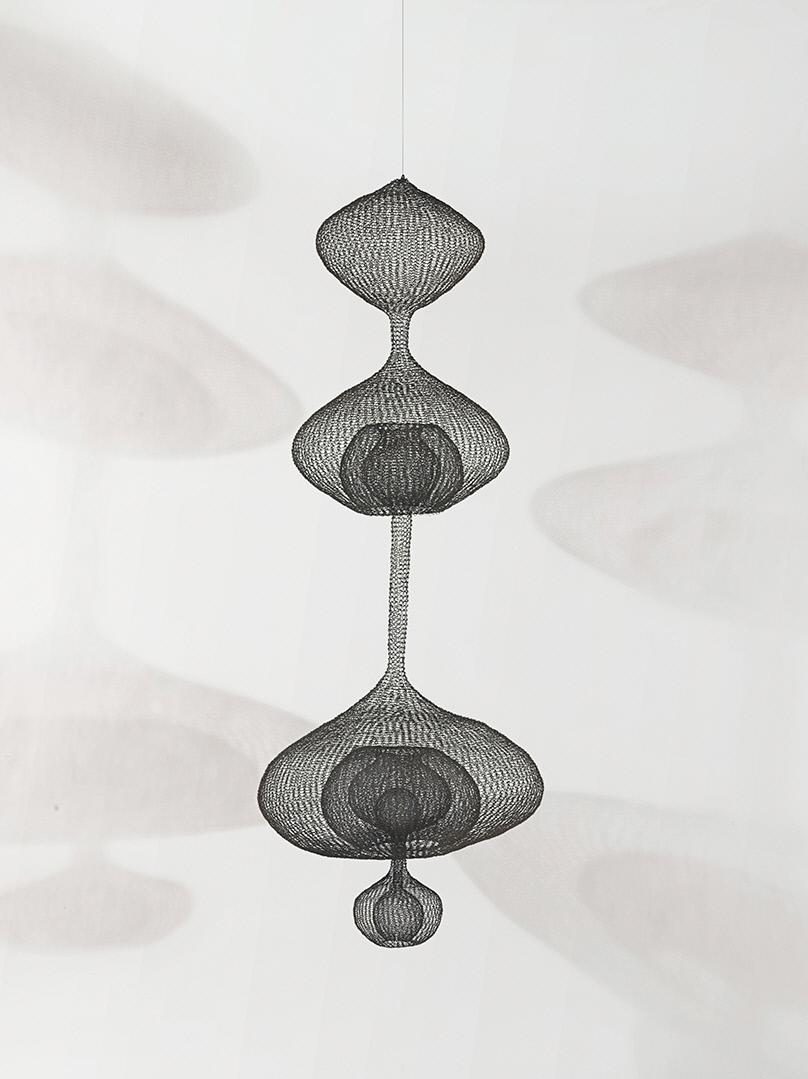 Suspended abstract black wire mesh sculpture with geometric shapes casting intricate shadows
