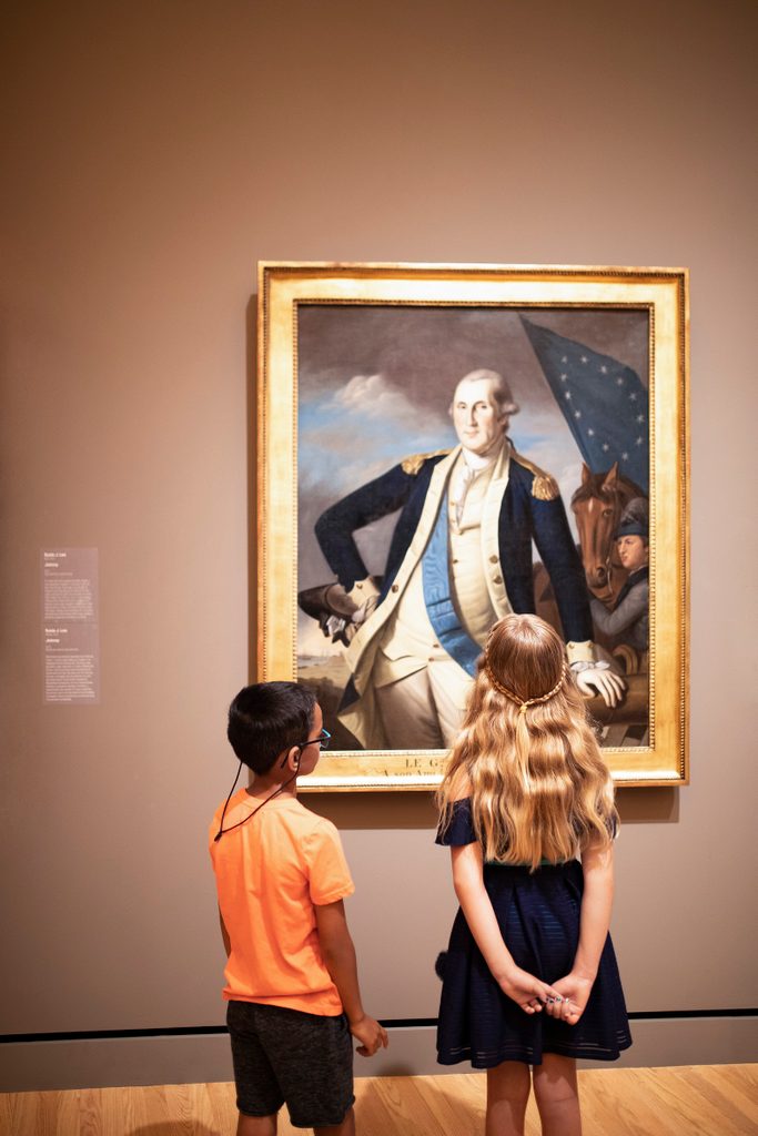 a young girl and boy look at a portrait of george washington by charles willson peale in the crystal bridges gallery