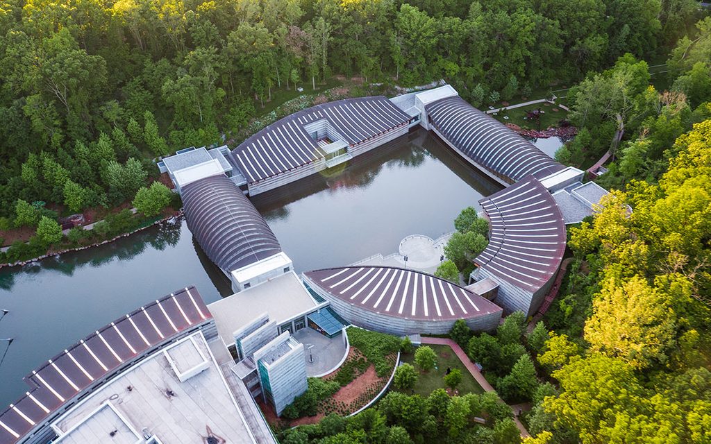 Aerial view of a modern museum complex with curved roofs, central pond, surrounded by greenery.