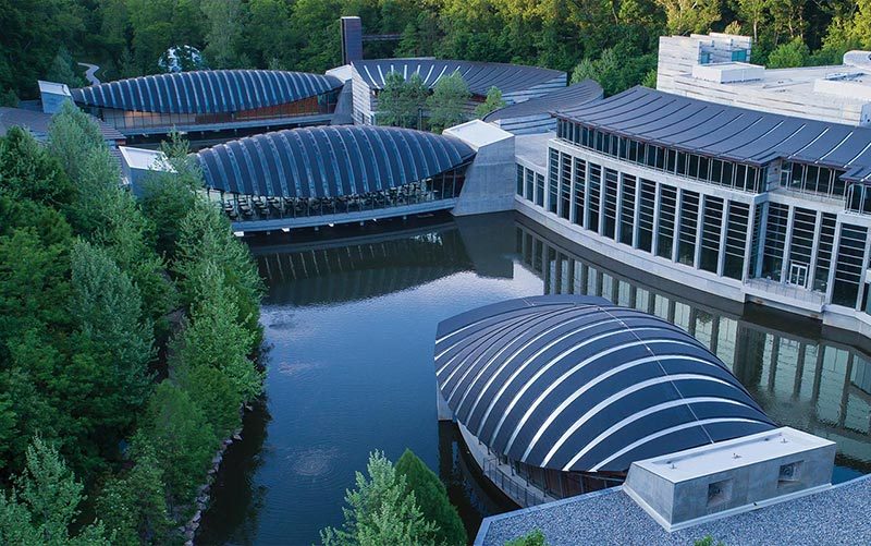 Curved glass buildings around a reflective pond, surrounded by greenery