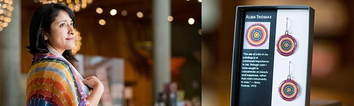 Woman in colorful shawl near a display box with Alma Thomas-inspired circular earrings.