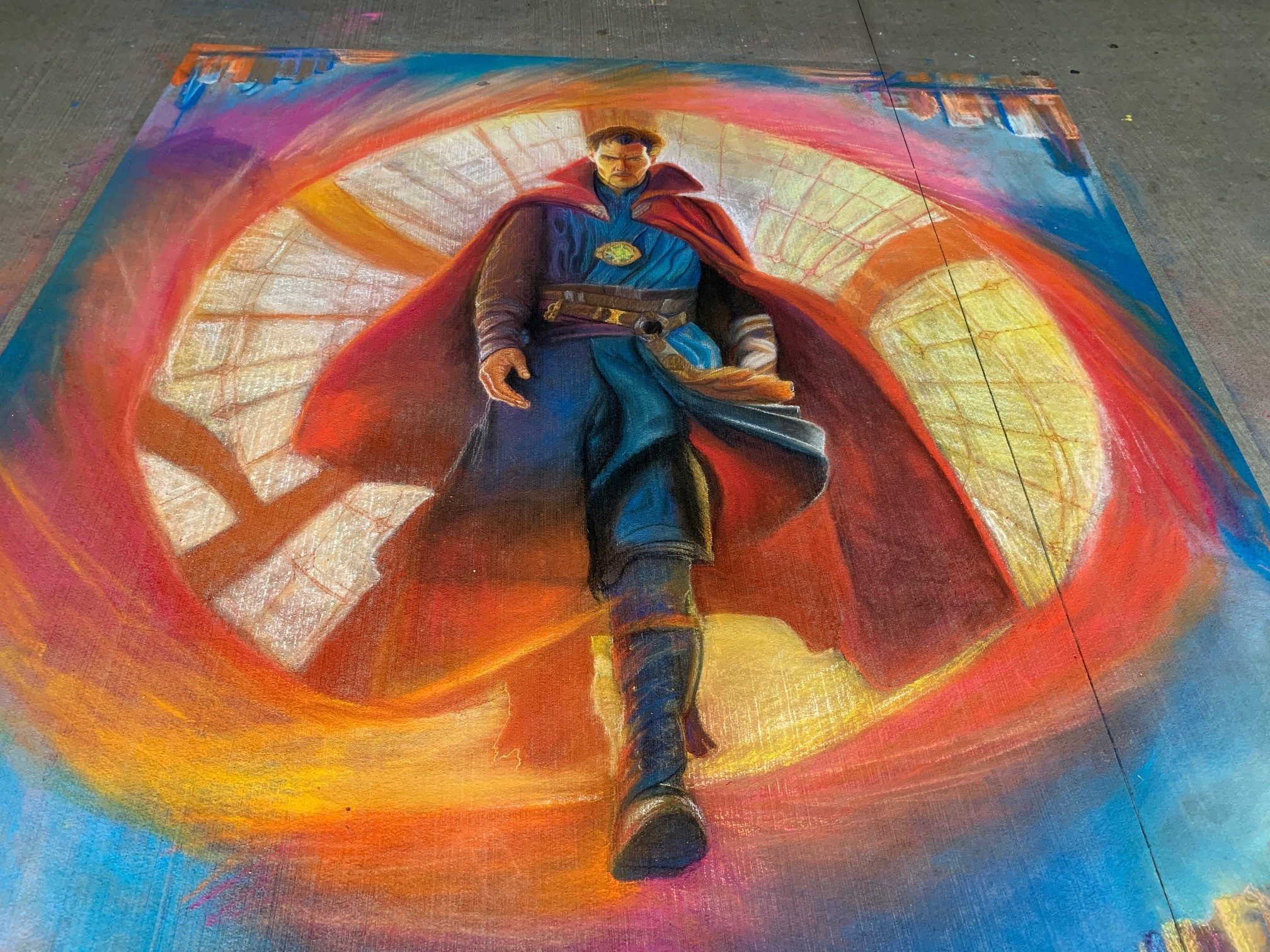 Chalk art on pavement of character in red cape walking through a vibrant glowing portal.