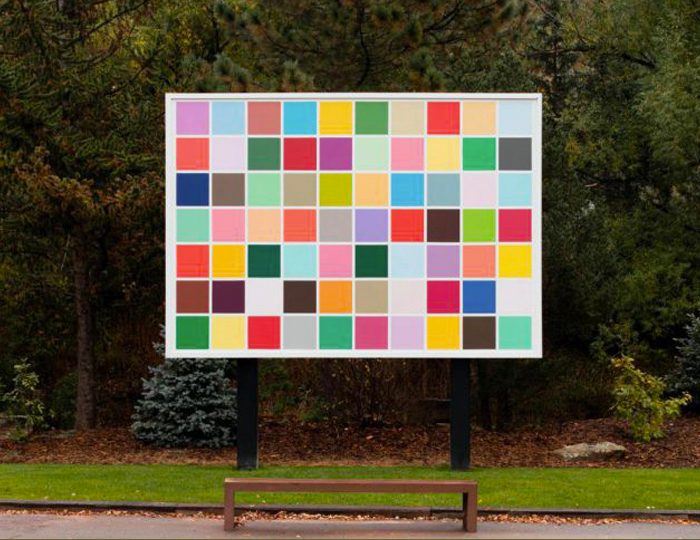 Outdoor sign with colorful squares in park setting, trees and bench in front.