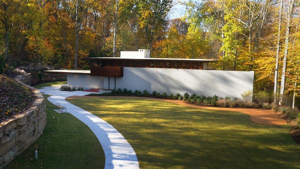 Modern, flat-roofed house in a wooded area with fall colors and a curved white path.