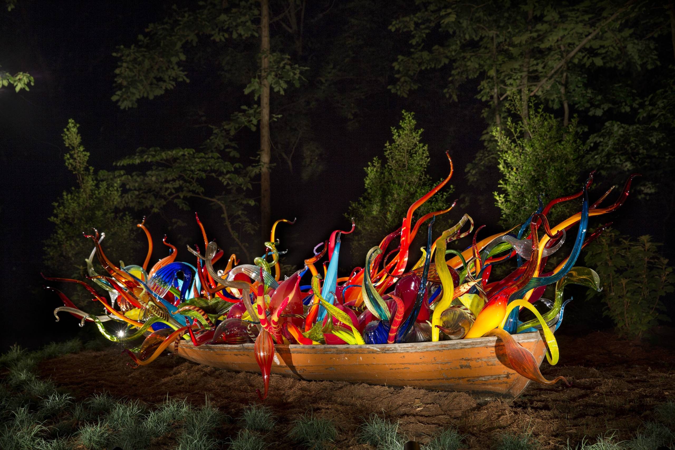Wooden boat with colorful glass sculptures in forest.