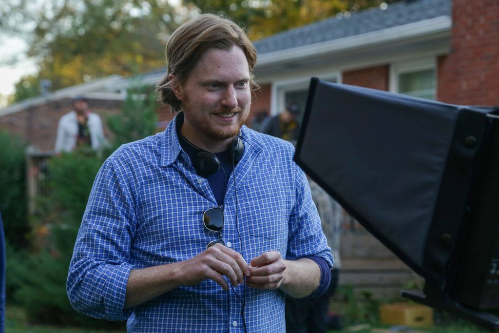 a man with headphones around his neck looks into a film camera