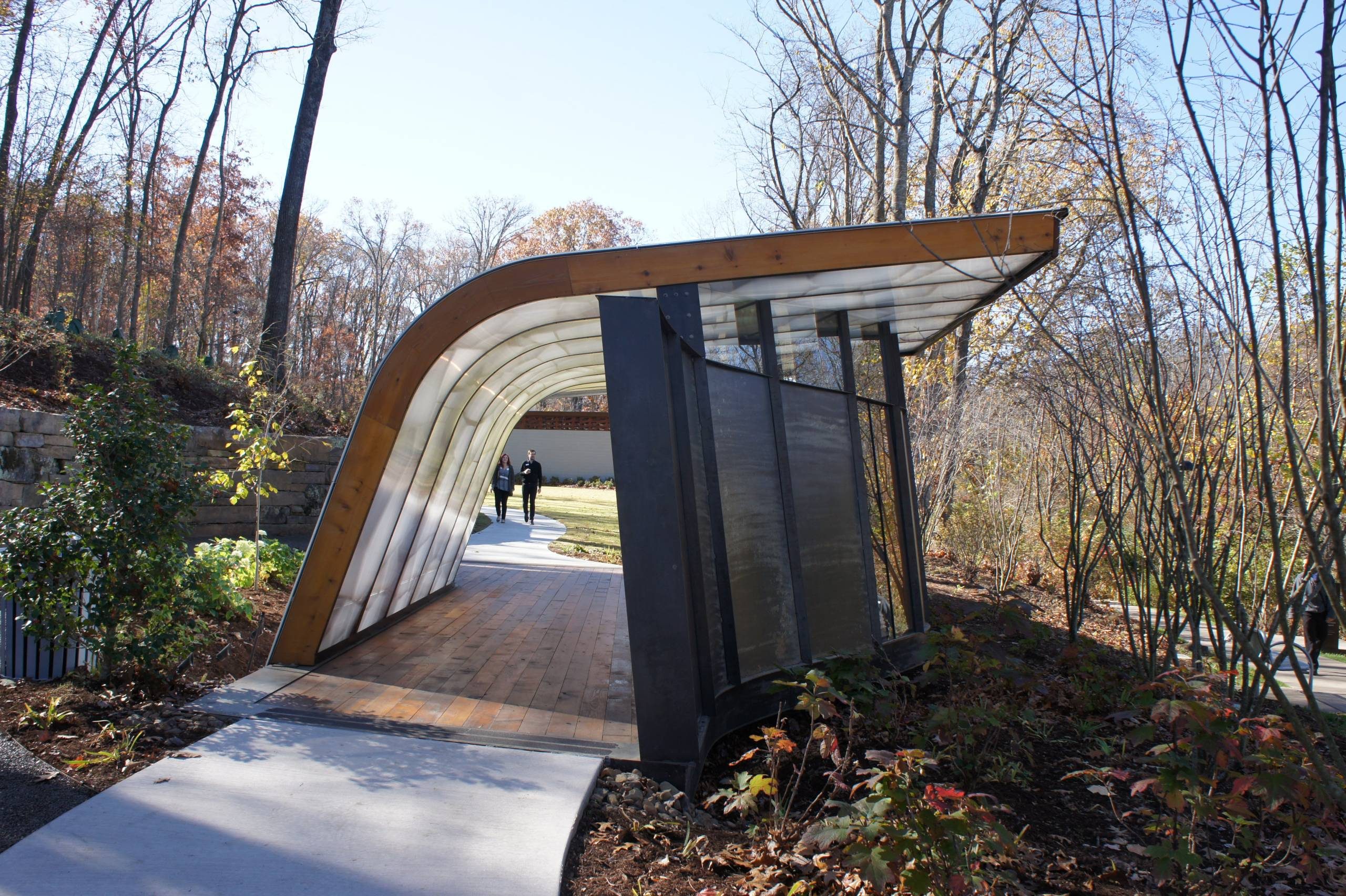 Curved metal walkway in autumn woods with two people approaching along the path.