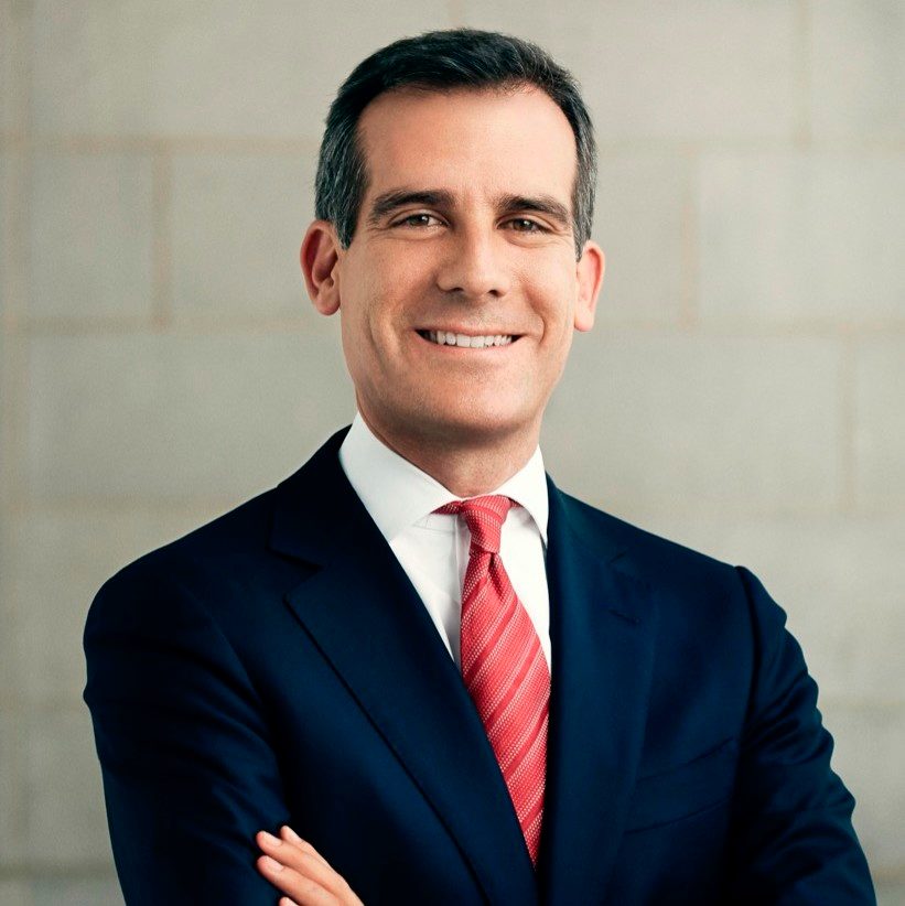 Person in dark suit with red striped tie, arms crossed, smiling against neutral background.