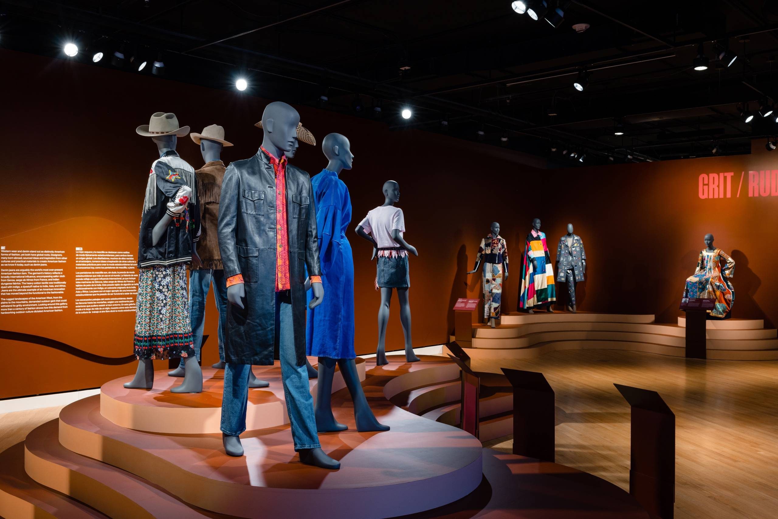 a bright red-orange shirt and black leather jacket on a mannequin in a gallery space among other dressed mannequins in outerwear