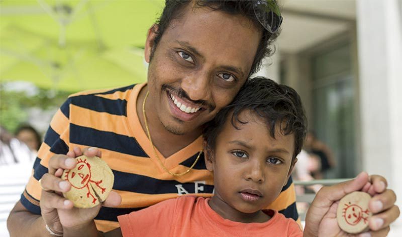 Man and child holding cookies with drawings in an outdoor area with green umbrellas.