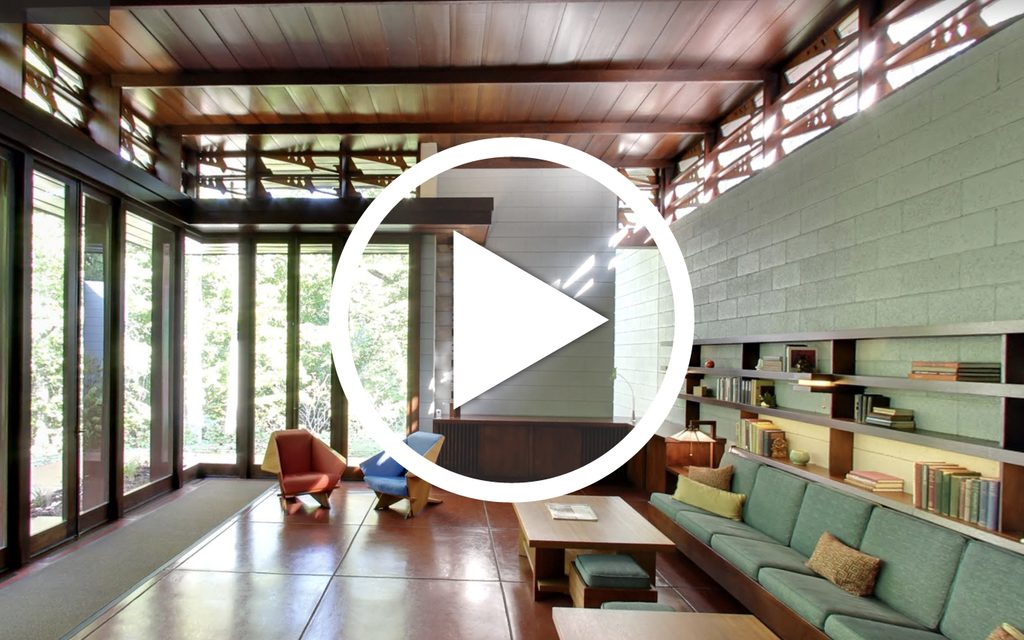 Modern living room with large windows, wooden furnishings, colorful seating, and natural light.