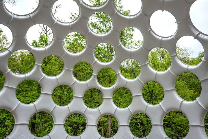 Geometric structure with circular openings contrasted by lush green trees in the background.