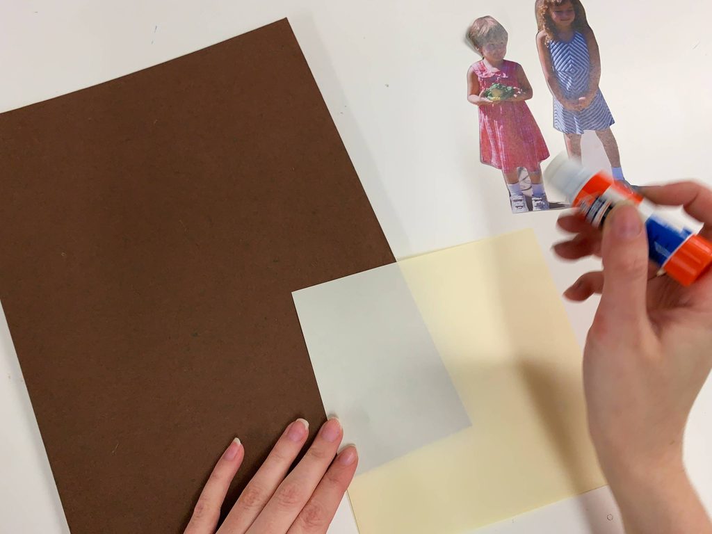 a pair of hands gluing a white piece of paper to a brown piece of paper with glue stick