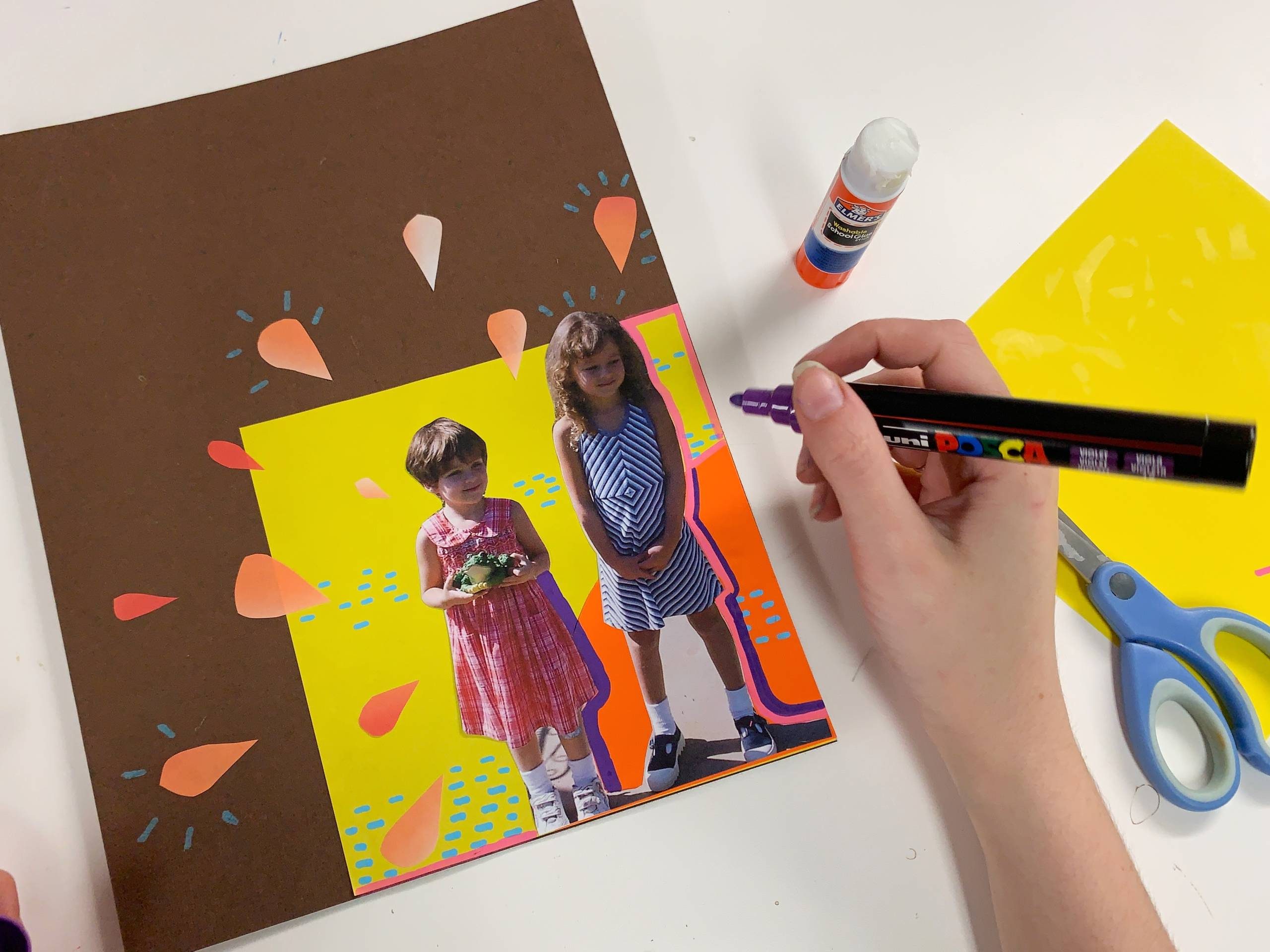 a pair of hands decorating a piece of paper decorated with orange teardrops and a photo of two young girls with a marker