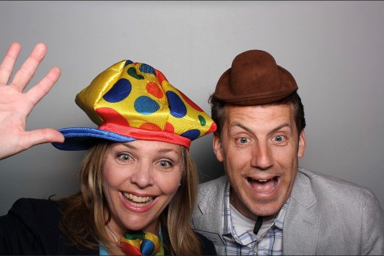 two staff members pose in a photo booth with silly hats