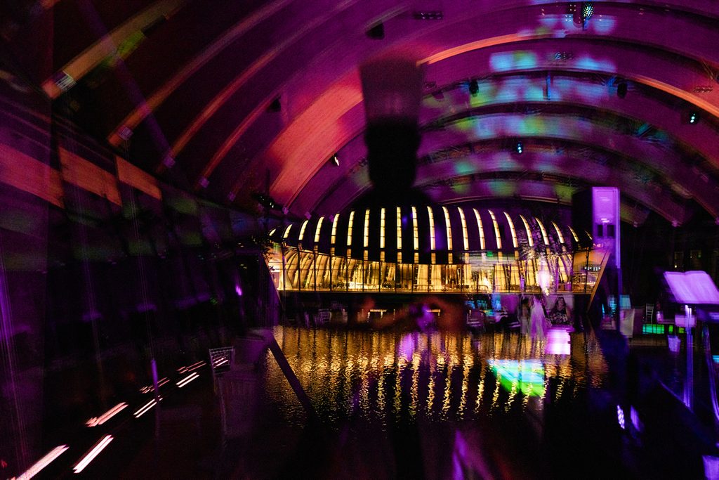 Curved ceiling with colorful lighting reflecting on water inside a vibrant building.