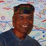 Person in patterned hat and dark shirt smiling in front of colorful abstract background.