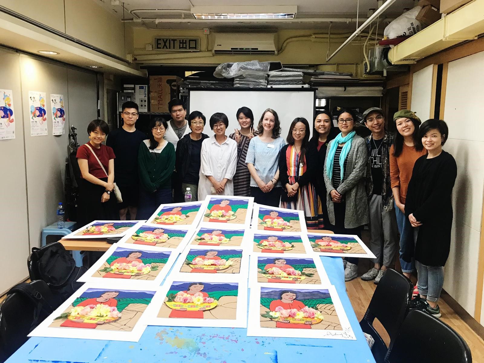 Group posing indoors with table displaying colorful artworks of a person and flowers.