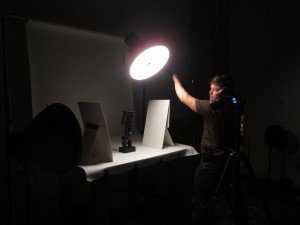 Person adjusting lighting in a photography studio with a camera on a tripod aimed at a table.
