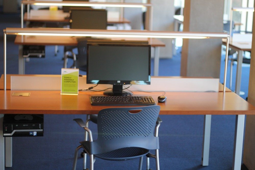 Study station with computer, keyboard, mouse on wooden desk; family-friendly sign visible.