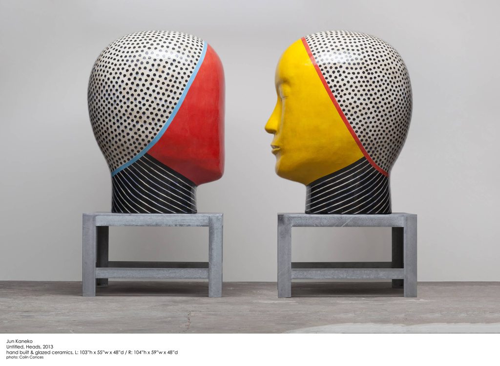 Two colorful head sculptures with polka dots, on metal stands, facing each other.