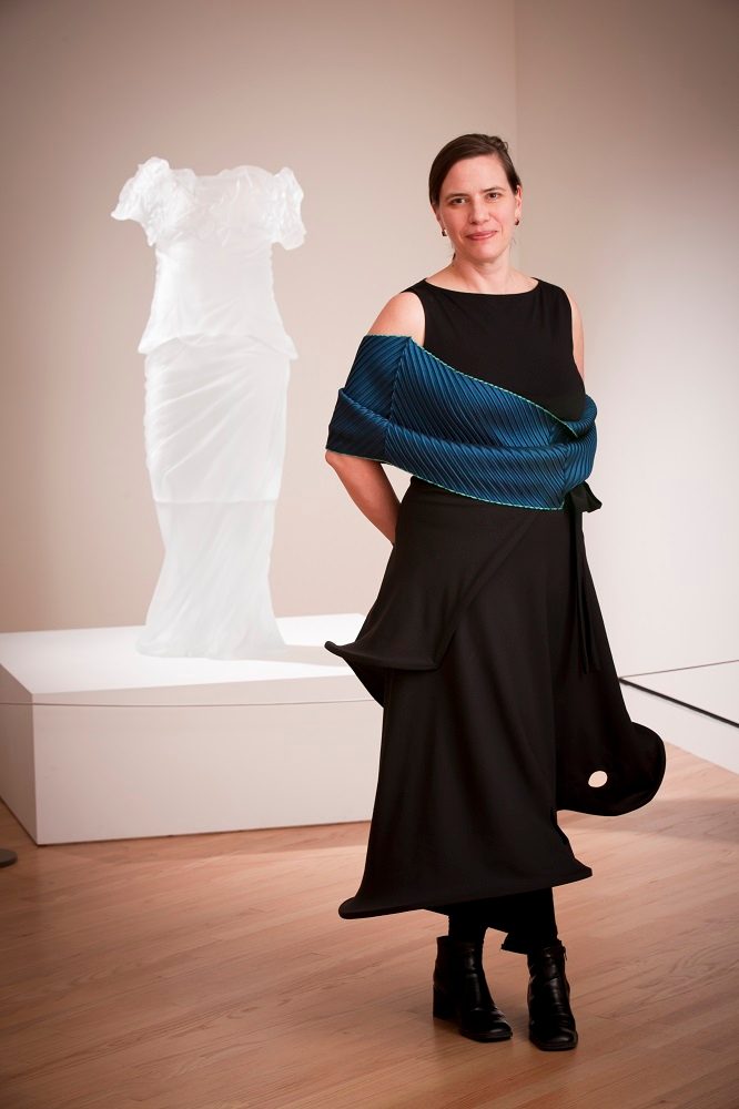 Woman in a black dress with blue wrap in an art gallery with a white sculpture on a pedestal.