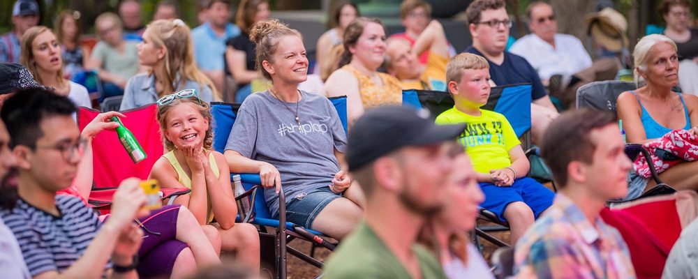Outdoor gathering with people seated on folding chairs at a casual social event.