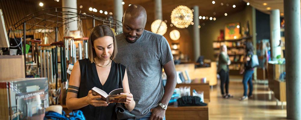Man and woman browsing a book in a well-lit store with modern decor and other shoppers.