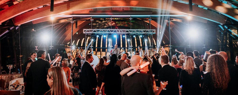 Indoor event with band on stage, bright lights, modern architecture, and formally dressed audience.