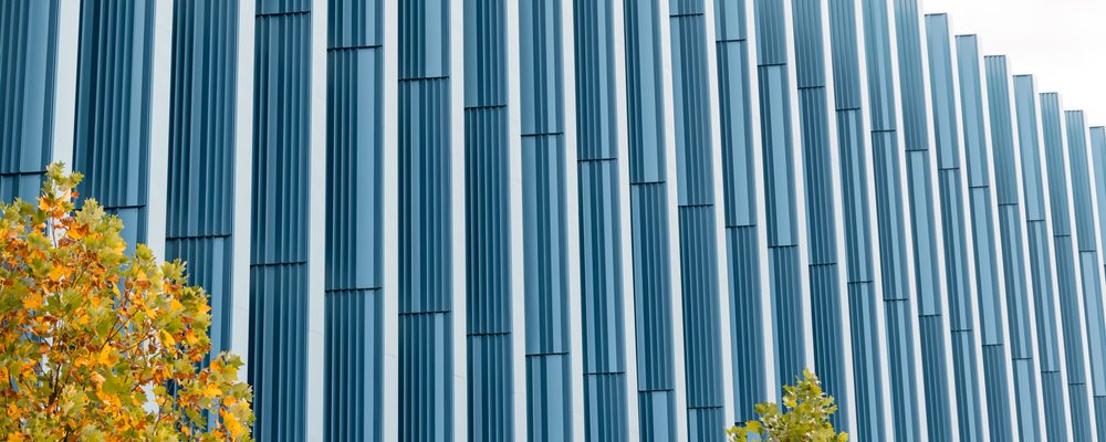 Tall building with blue panels, foreground trees with green and orange leaves.