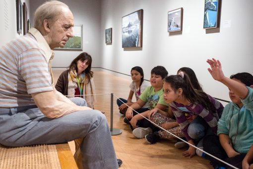 Children observe a lifelike statue of an elderly man in an art gallery setting.