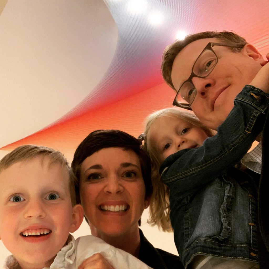 a staff member poses with her family underneath the colorful string artwork in the galleries