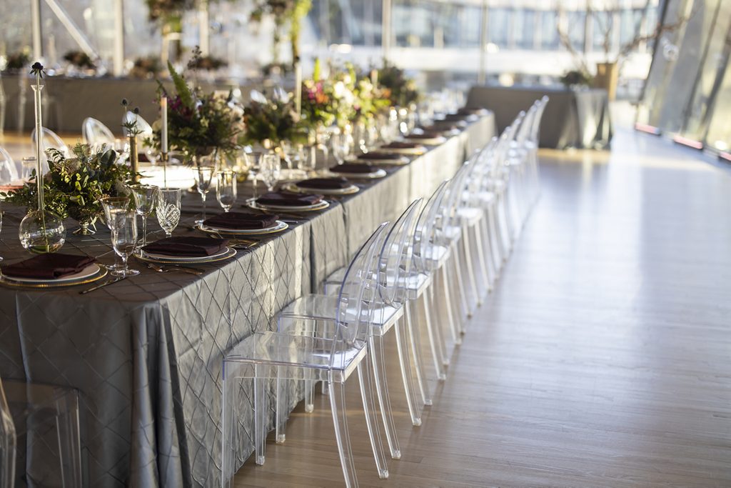 Elegant dining table with floral centerpieces, quilted tablecloth, and transparent chairs.
