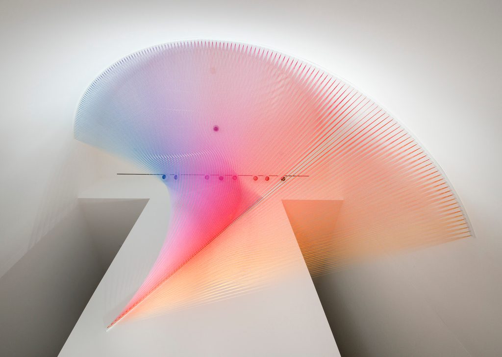 Colorful strings form a sweeping arc in a modern space, creating a blue, pink, and orange gradient.