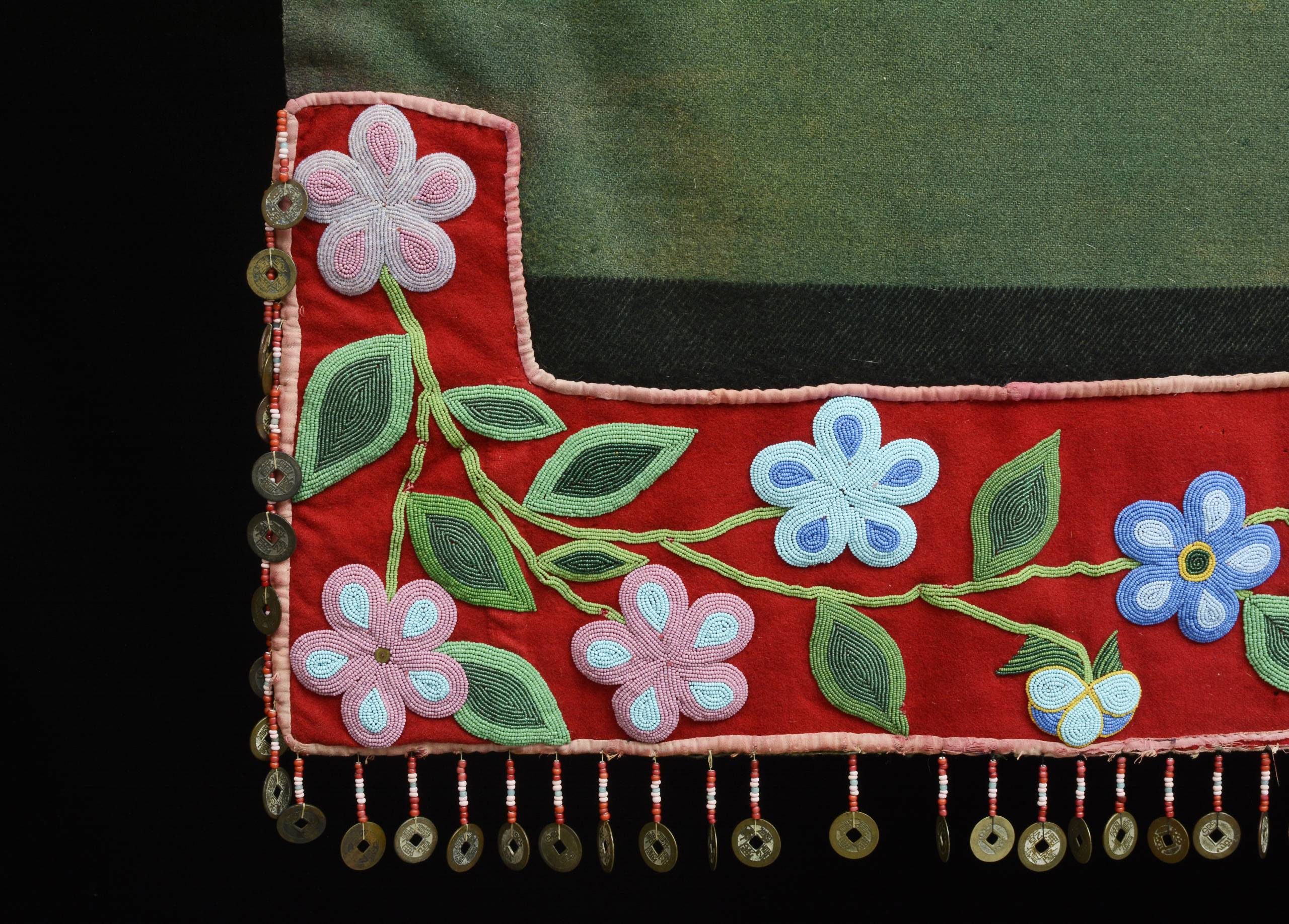 Textile with red border, pastel floral embroidery, green leaves, beads, and circular ornaments.