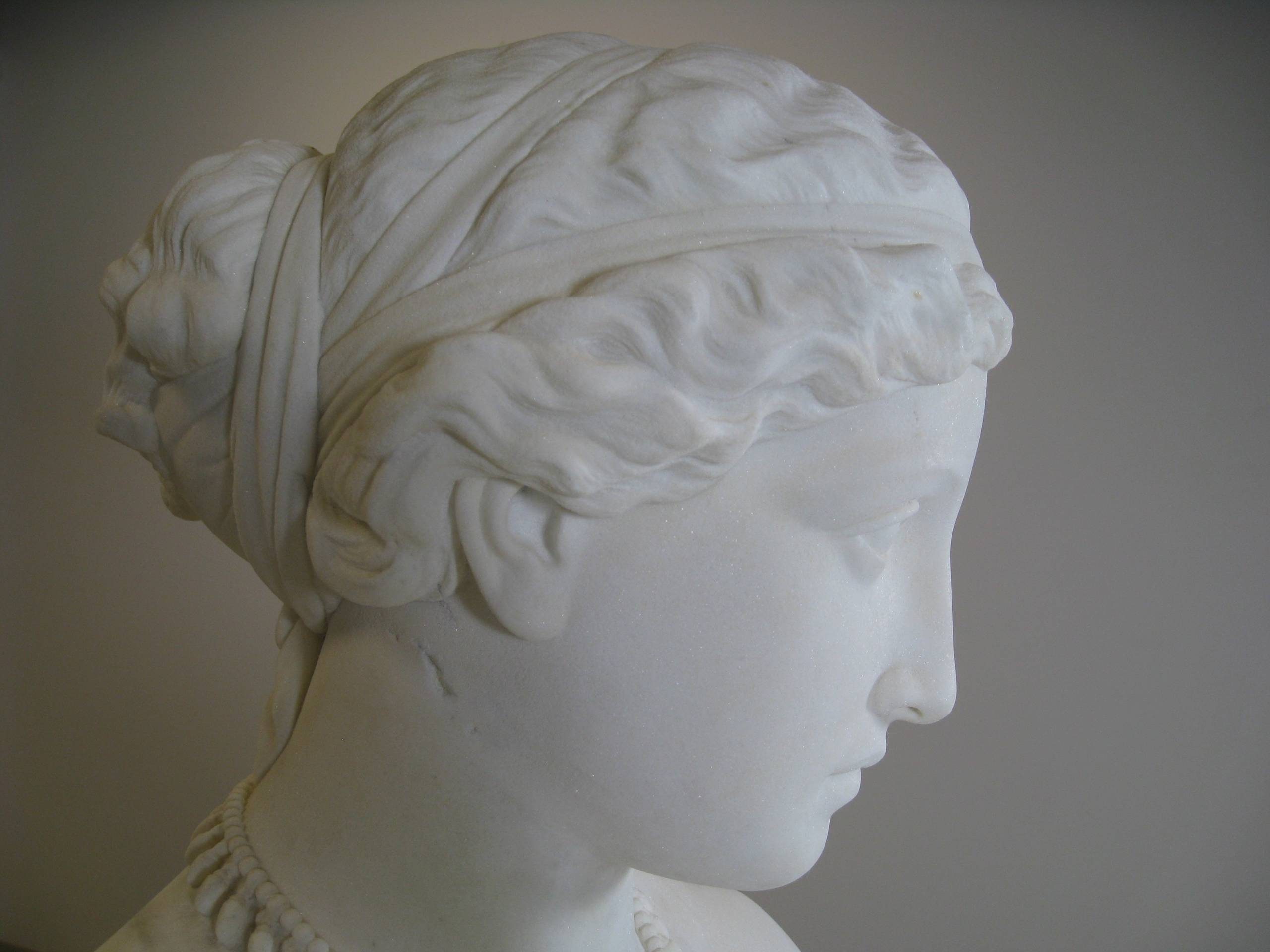 Marble sculpture of a woman's profile with detailed features and a headband, wearing a necklace.