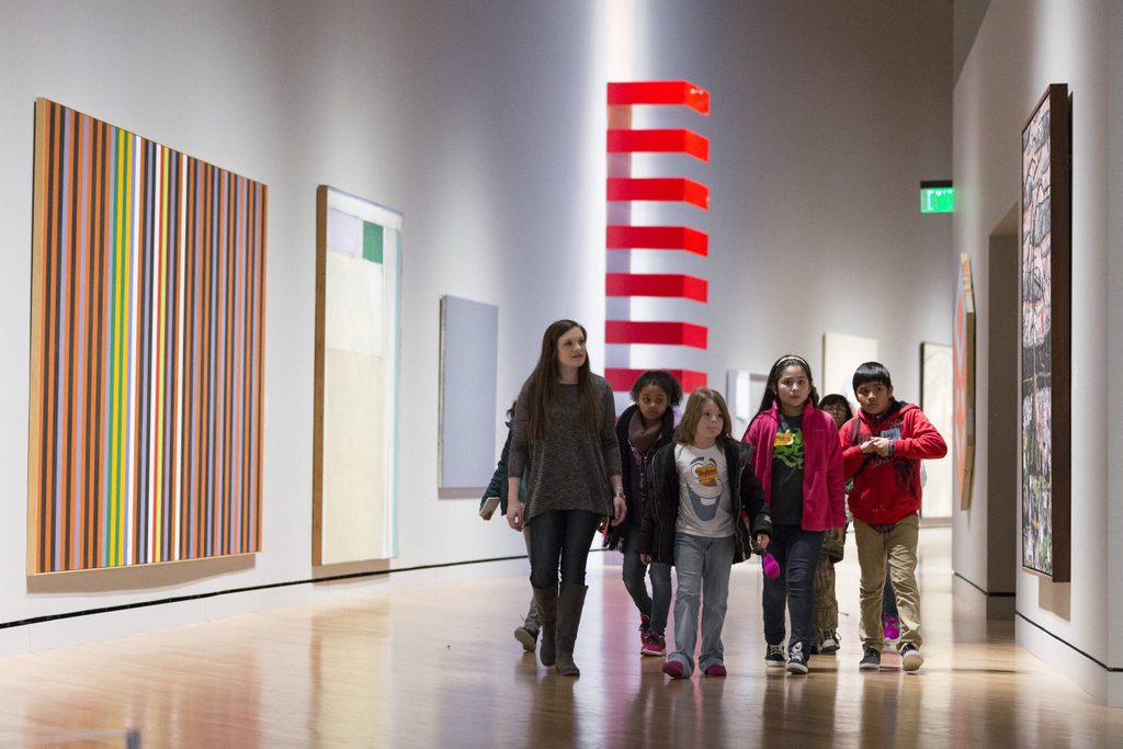 Children and an adult exploring a modern art gallery hallway with colorful abstract paintings.