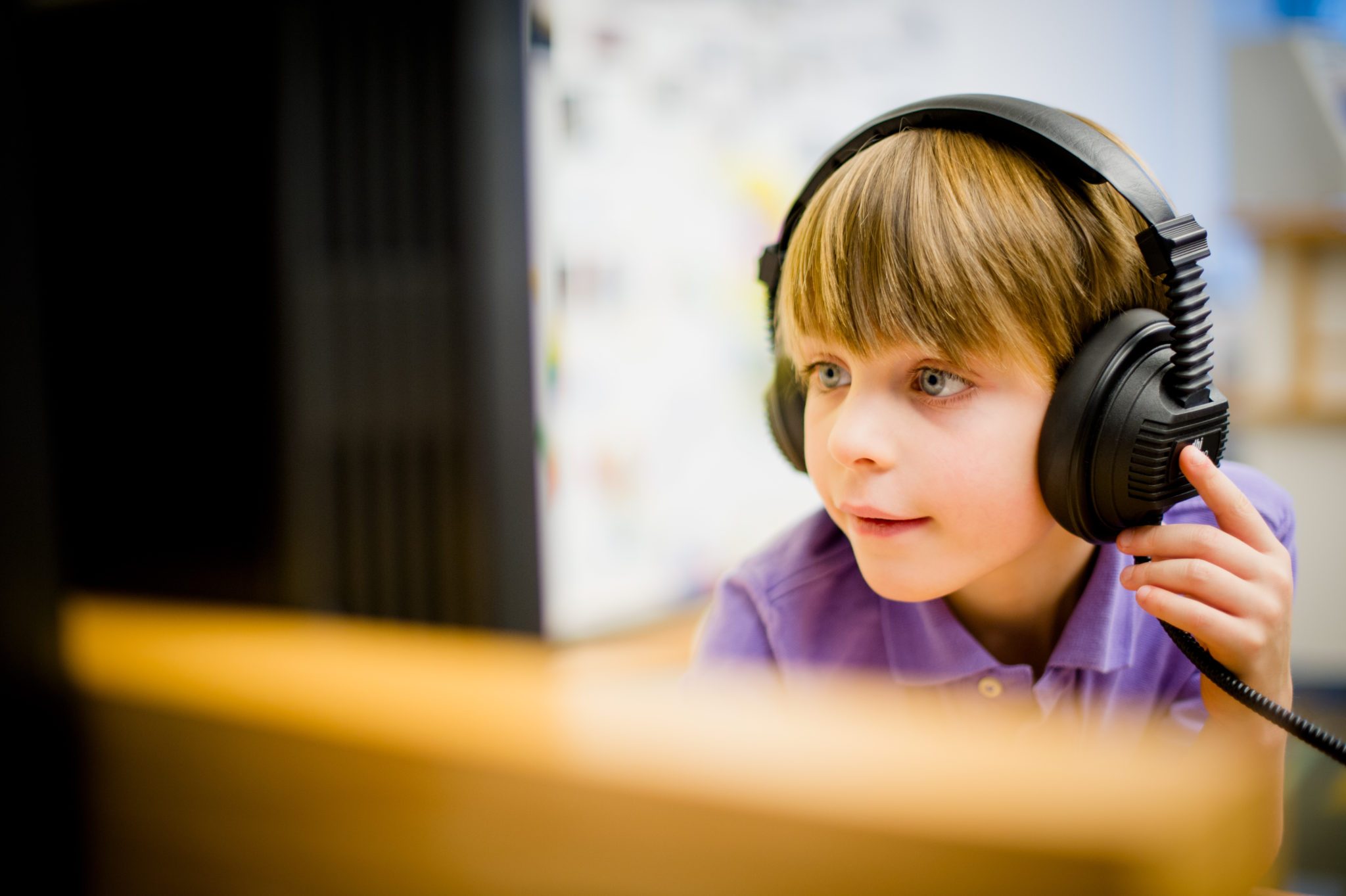 Child with large headphones looking at a computer screen in a bright indoor setting.
