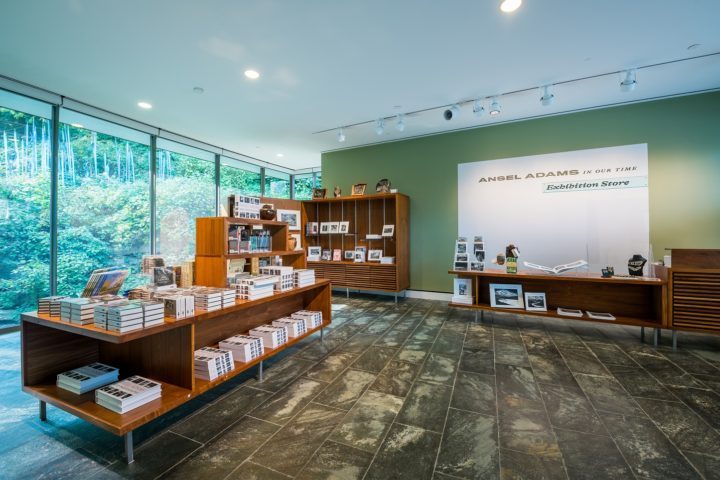Exhibition store with books and photos, large windows, greenery, stone floor, Ansel Adams signage.