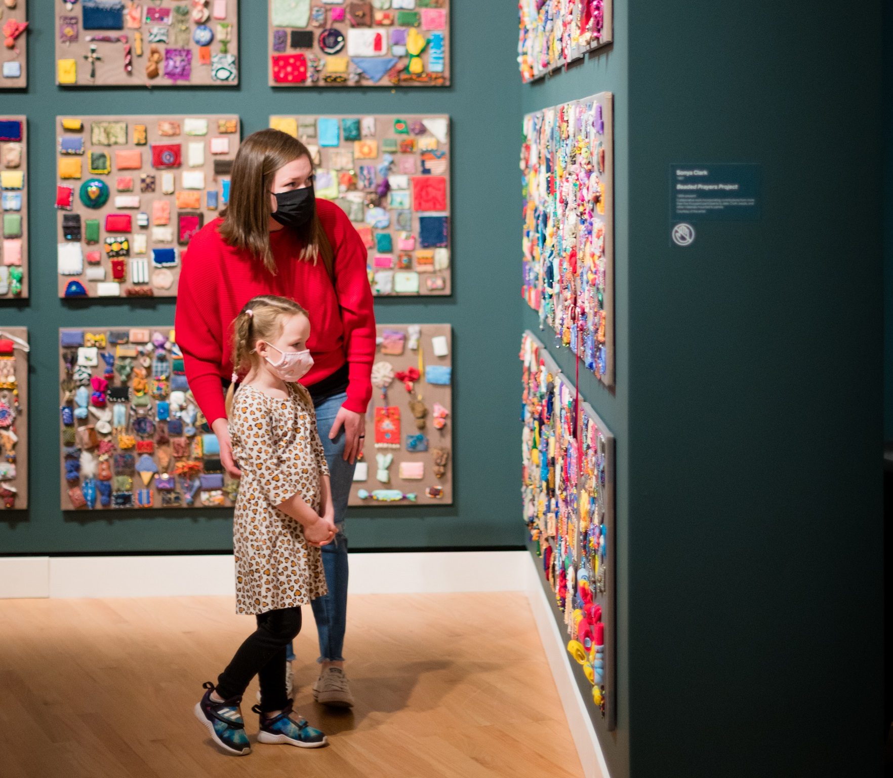 Woman and girl wearing masks viewing colorful wall art in a well-lit gallery.