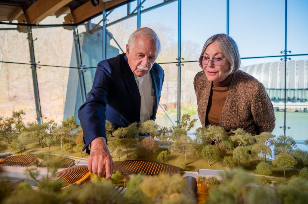 Older man and woman examining an architectural model with trees indoors near large windows.