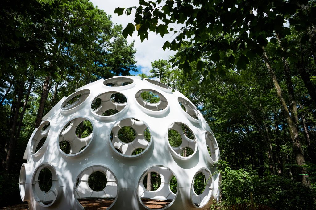 a white dome with circular windows all around it tucked beneath trees on both sides