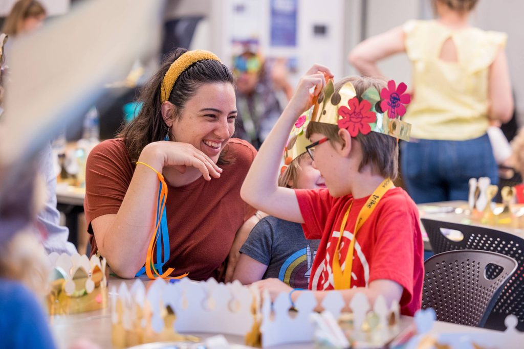 a mother and her son look at each other smiling while making a paper crown and art crafts in a studio