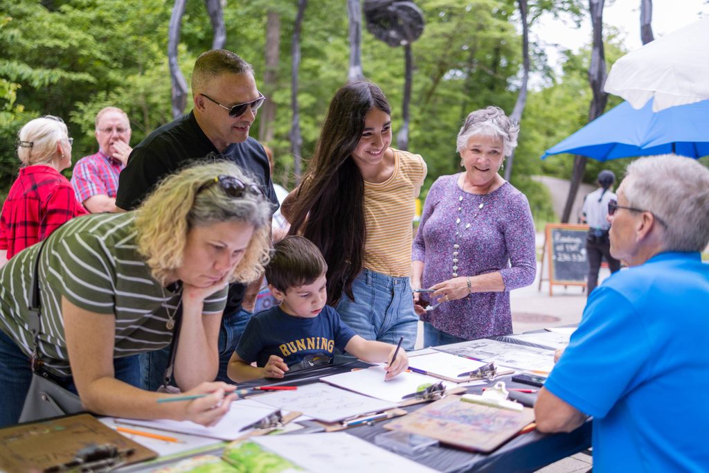 A family stops to chat with a partner at an outdoor event at Crystal Bridges