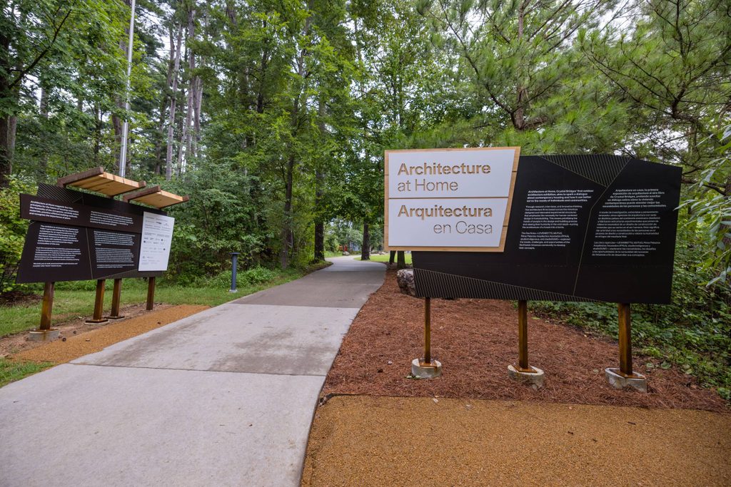 an outdoor walking path featuring a panel with information about Architecture at Home, an outdoor architecture exhibition